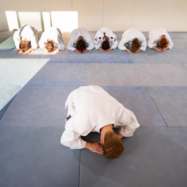 Gruppe von Aikido-Praktizierenden, die in gebückter Haltung auf blauen Matten im Dojo stehen.