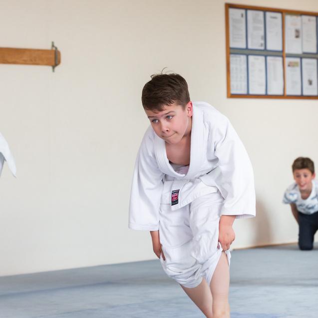 Vier Jungen in weißen Judoanzügen üben auf einem blauen Mattenboden, einer beugt sich nach vorne.