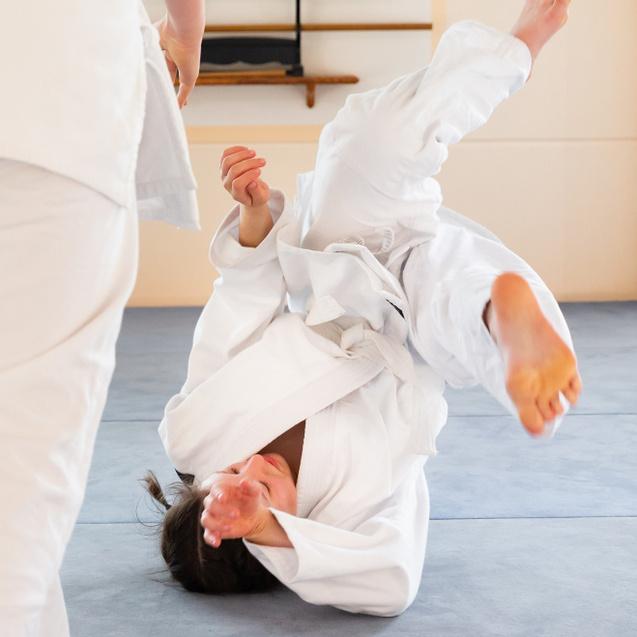Zwei Judokas in weißen Anzügen üben einen Wurf, während einer verletzt auf dem Boden liegt.