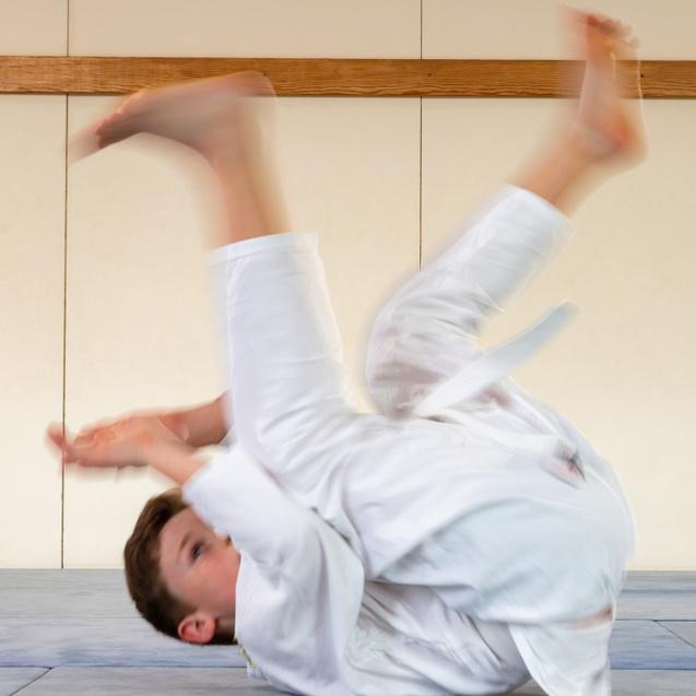 Junge im weißen Judoanzug führt eine Rolle auf der blauen Judomatte aus.