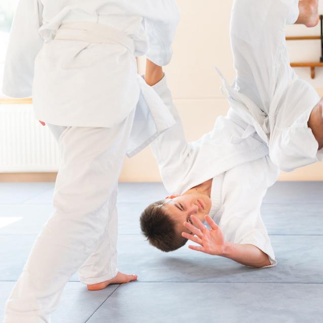 Junge in weißem Judogi führt einen Wurf aus, während er von einem anderen Judoka gehalten wird.