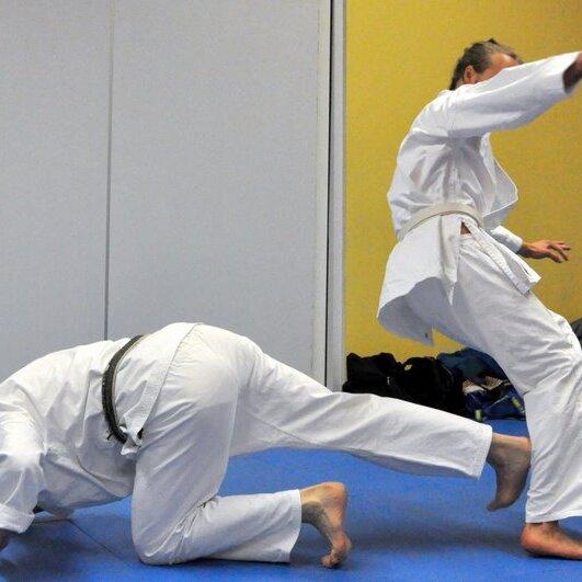 Zwei Judoka im Kampf, einer kniet und der andere führt einen Wurf aus, beide in weißen Judogis.