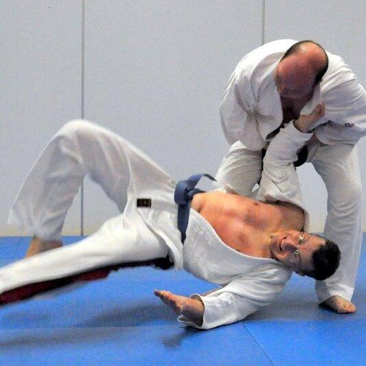 Zwei Judoka in weißen Anzügen kämpfen auf einer blauen Matte, während einer den anderen zu Boden wirft.