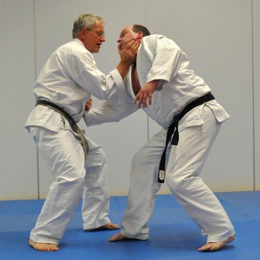 Zwei Männer in Judoanzügen kämpfen auf einer blauen Matte in einem Judotraining.