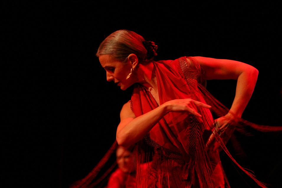 Eine Tänzerin in rotem Kostüm neigt sich zur Seite und richtet den Blick zum Boden.