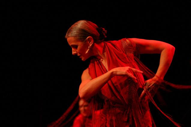 Eine T&auml;nzerin in rotem Kost&uuml;m neigt sich zur Seite und richtet den Blick zum Boden.