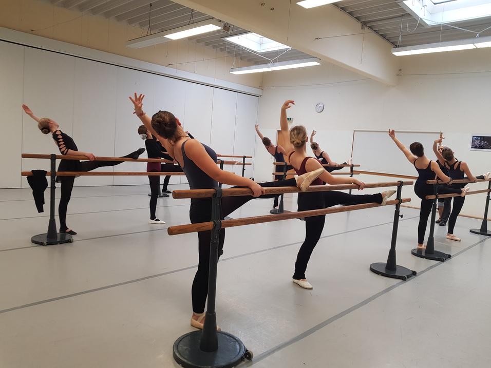 Balletttraining 2019 Ballettraining an der Stange. Ein Bein der Tänzerinnen liegt gestreckt auf der Stange, ein Arm wird über den Kopf geführt.