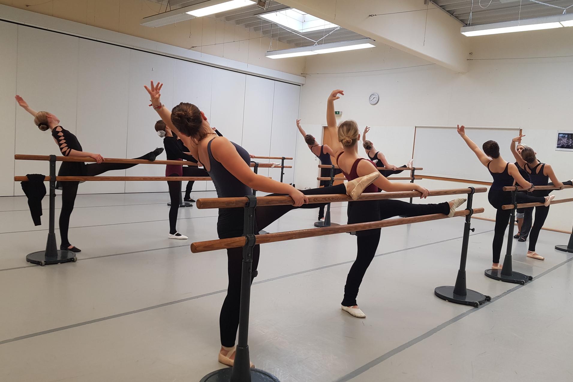 Balletttraining 2019 Ballettraining an der Stange. Ein Bein der Tänzerinnen liegt gestreckt auf der Stange, ein Arm wird über den Kopf geführt.