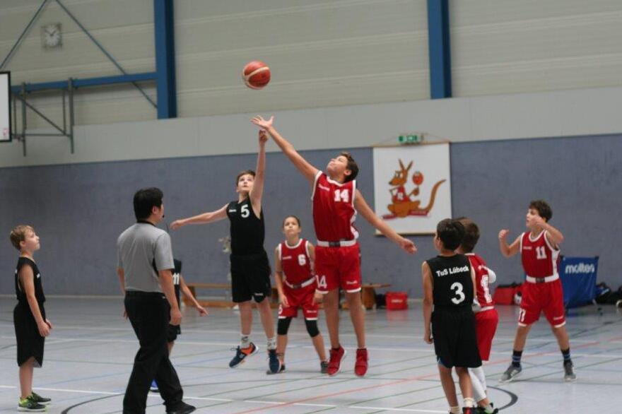 Zwei Basketballer kämpfen beim Sprungball um den zu tippenden Ball.