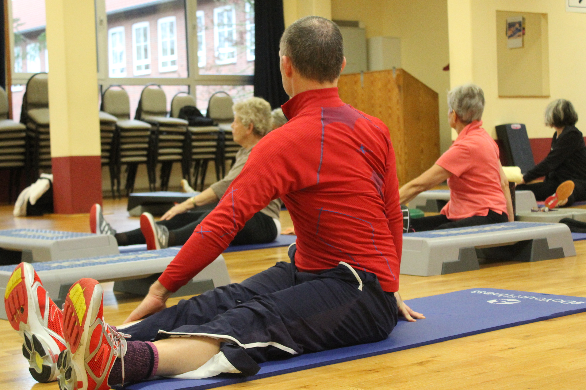 Teilnehmer der Core-Fitness Gruppe sitzen auf der Fitnessmatte und dehnen den unteren Rücken