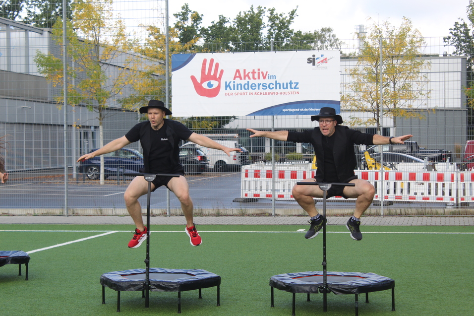 Zwei M&auml;nner in schwarzer Kleidung mit Hut springen jeweils auf einem Trampolin