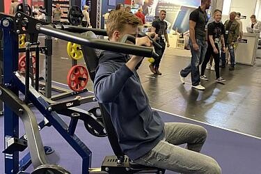 Ein junger Mann sitzt w&auml;hrend der Messe auf einem Fitnessger&auml;t und demonstriert die &Uuml;bung