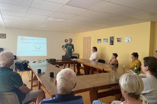 Personen sitzen um einen Tischkreis und schauen zum Referenten Sebastian David