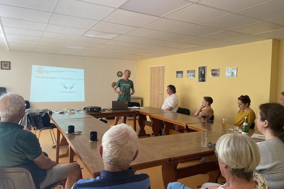 Personen sitzen um einen Tischkreis und schauen zum Referenten Sebastian David