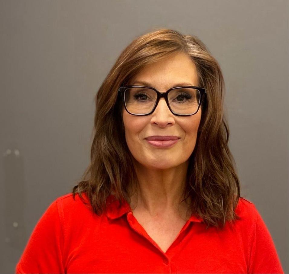 Frau mit langen, brünetten Haaren und Brille in rotem Polo-Shirt vor grauem Hintergrund.