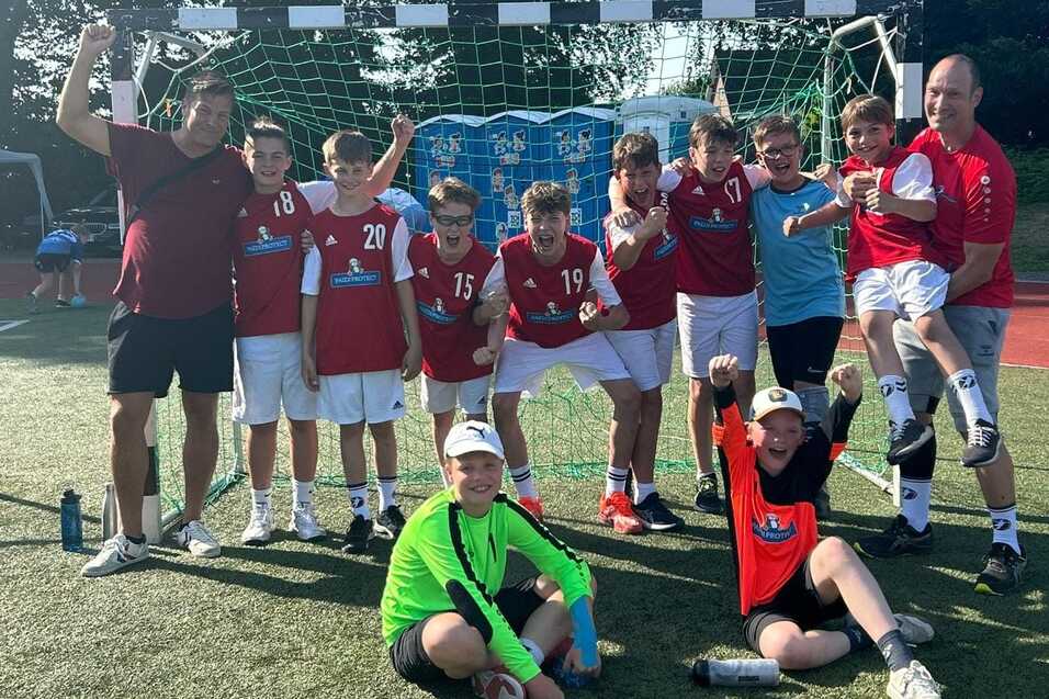 D-Jugend feiert Turniersieg Die männliche Handball D-Jugend feiert als Gruppe jubelnd den Titelgewinn vor dem Handballtor auf dem Rasensportplatz der Tus Aumühle-Wohltorf.