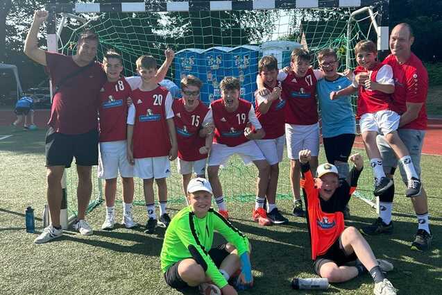 Die männliche Handball D-Jugend feiert als Gruppe jubelnd den Titelgewinn vor dem Handballtor auf dem Rasensportplatz der Tus Aumühle-Wohltorf.