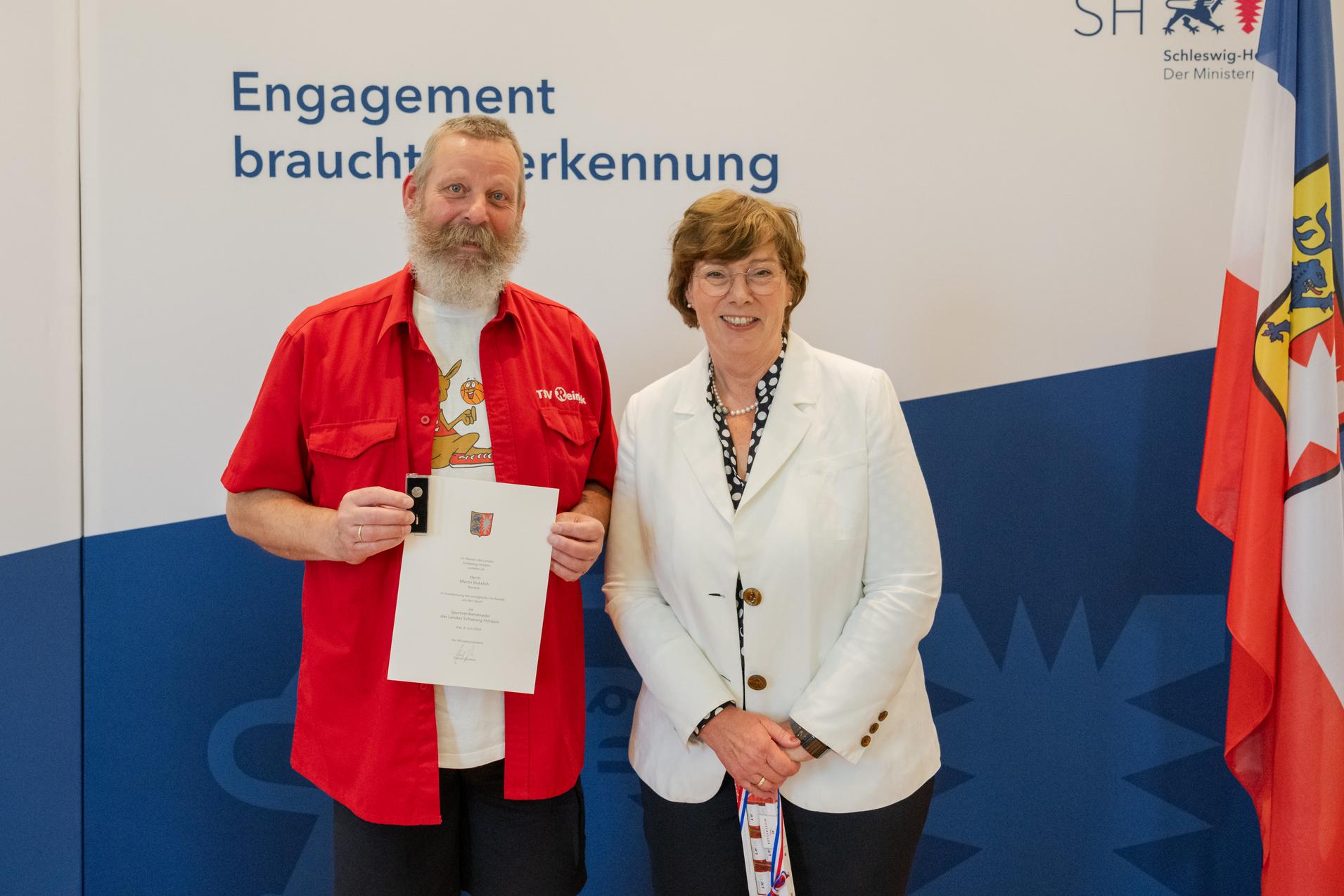 Sportverdienstnadel Martin Bokeloh 2024 Sportministerin Frau Dr. Sabine Sütterlin-Waack zeichnet Martin Bokeloh mit der Sportverdienstnadel des Landes aus