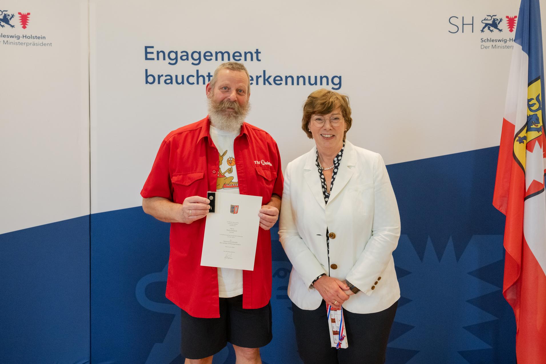 Sportverdienstnadel Martin Bokeloh 2024 Sportministerin Frau Dr. Sabine Sütterlin-Waack zeichnet Martin Bokeloh mit der Sportverdienstnadel des Landes aus