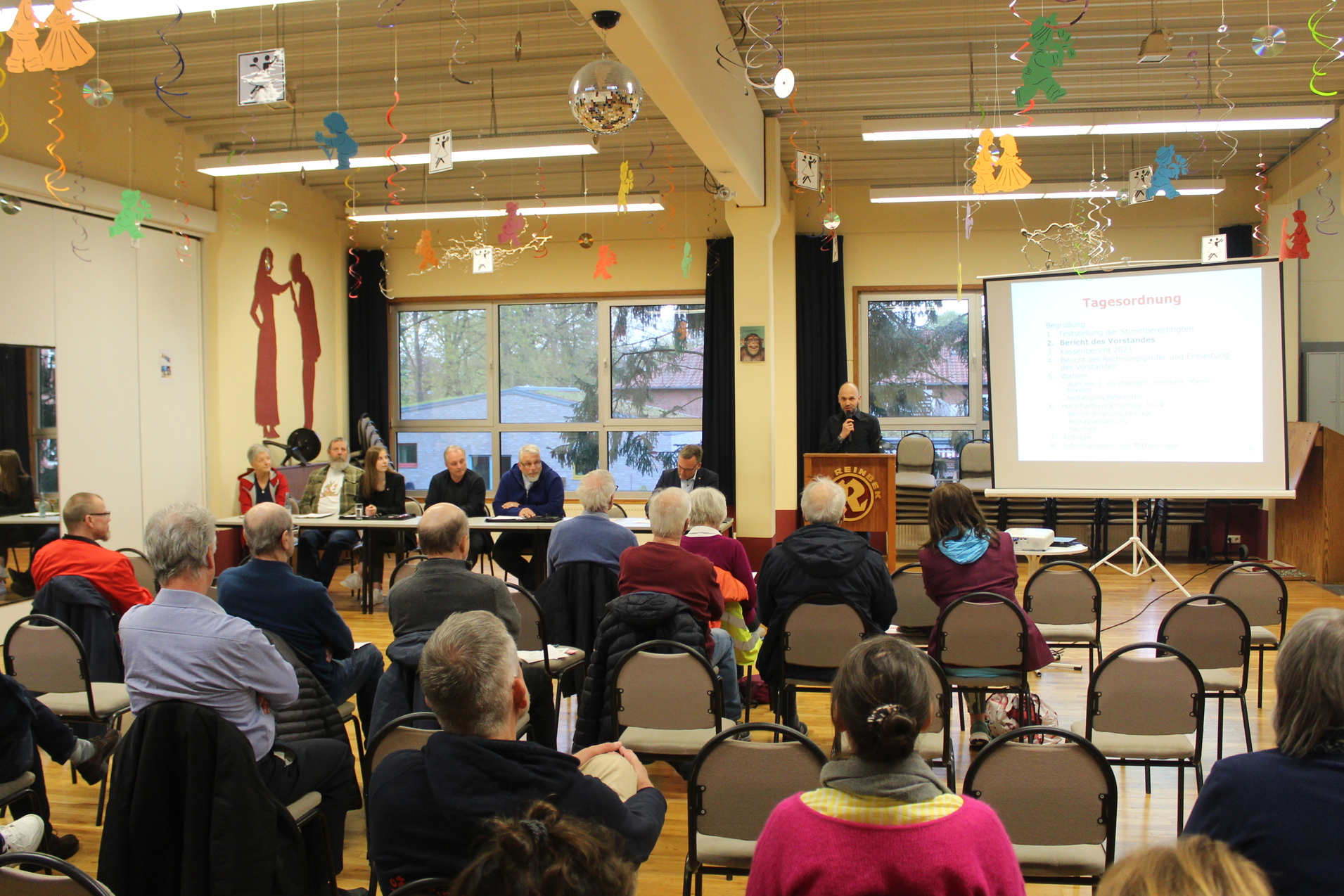Foto aus dem Rücken der Delegierten mit Blick zum Rednerpult und dem Vereinsvorstand