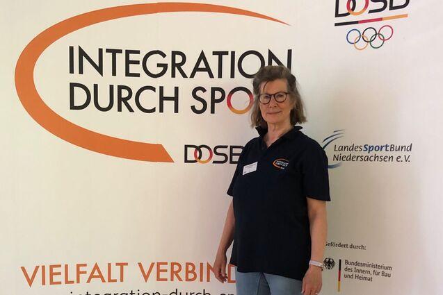Integrationslotsin Babette Rackwitz-Hilke steht vor dem Fotobanner Integration durch Sport.