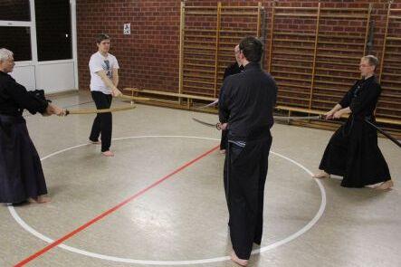 Fünf Iaido-Kämpfer stehen im Kreis in einer Halle und üben den Umgang mit Schwertern