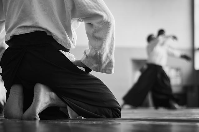 Kniende Person vorne schaut im Hintergrund kämpfenden Personen zu