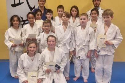 Teilnehmer der Gürtelprüfung in ihren Anzügen mit Urkunden nebeneinander.