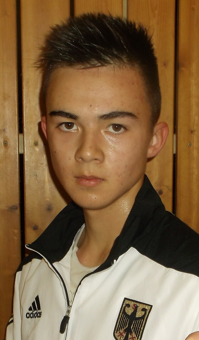 Junger Sportler mit nassem Haar und ernstem Gesichtsausdruck, trägt eine Jacke mit dem deutschen Nationalwappen.