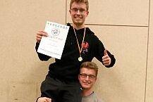 Nikolai Wuttke - Deutscher Meister Kung Fu Nikolai Wuttke sitzt auf der Schulter eines Mannes und präsentiert die Siegerurkunde und Medaille