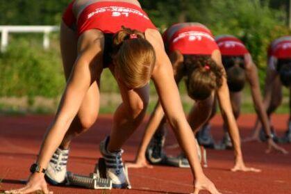 Startposition Wettkampf Vier junge Frauen in roten Oberteilen in Startposition für einen Lauf.