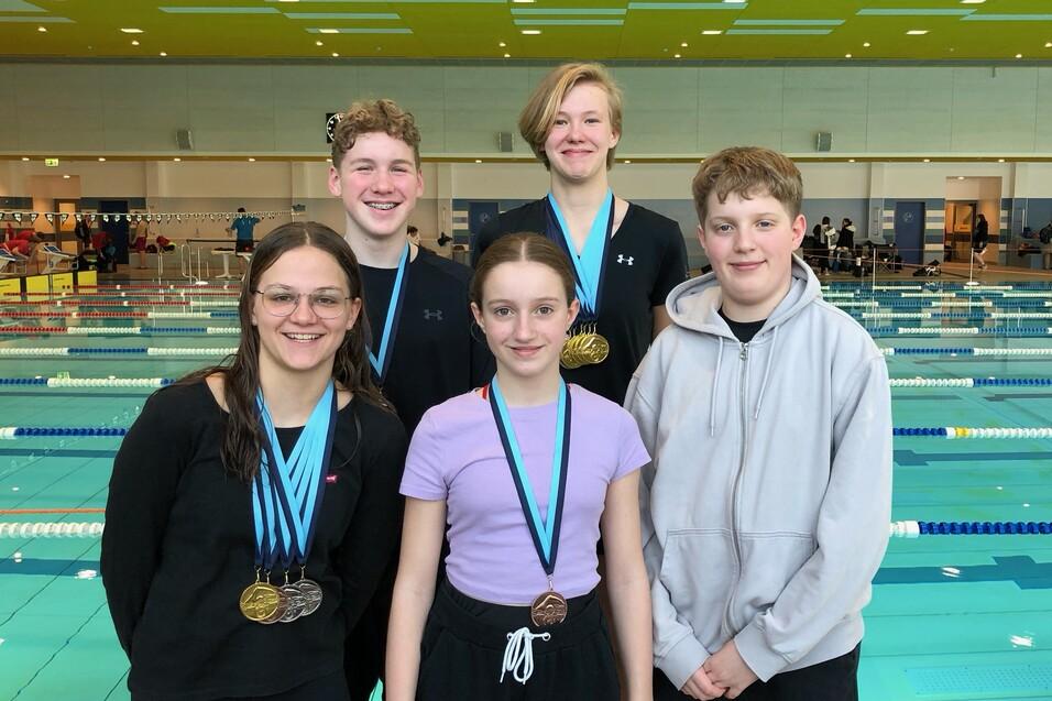 2024-Huchtinger-Championat-in-Bremen 5 SchwimmerInnen in Sportkleidung nebeneinander vor den Schwimmbahnen. Vier haben Medaillen um den Hals hängen.