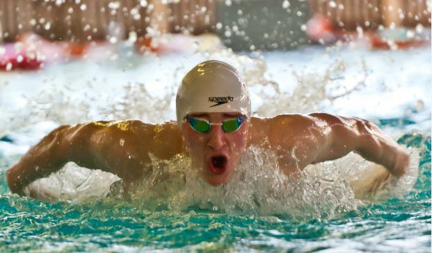 Schwimmer mit weißer Badekappe und weit geöffnetem Mund. Die Arme tauchen hinter den Schultern aus dem Wasser auf.