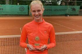 Merle Pukall mit Pokal vor einem Tennisnetz auf dem Platz.