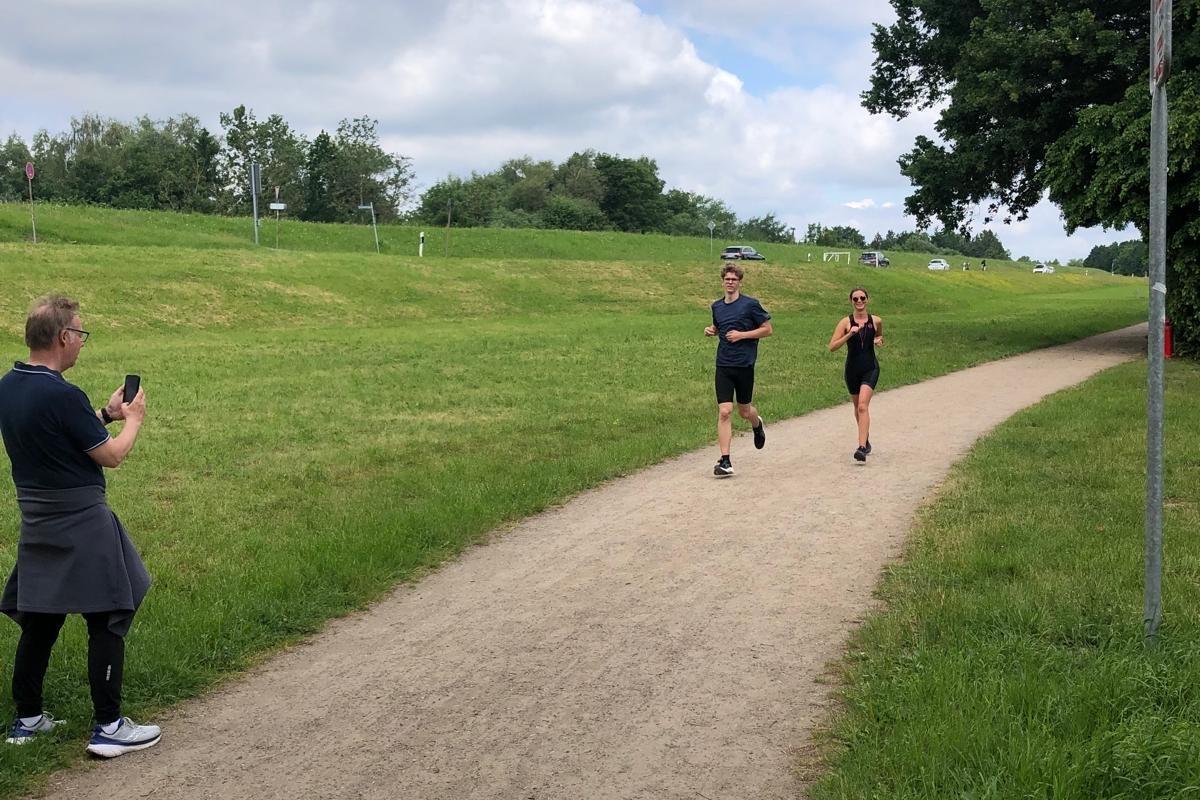 Probetriathlon 2026 Zwei Läufer auf der Strecke laufen auf ein am Wegrand stehende Person zu.