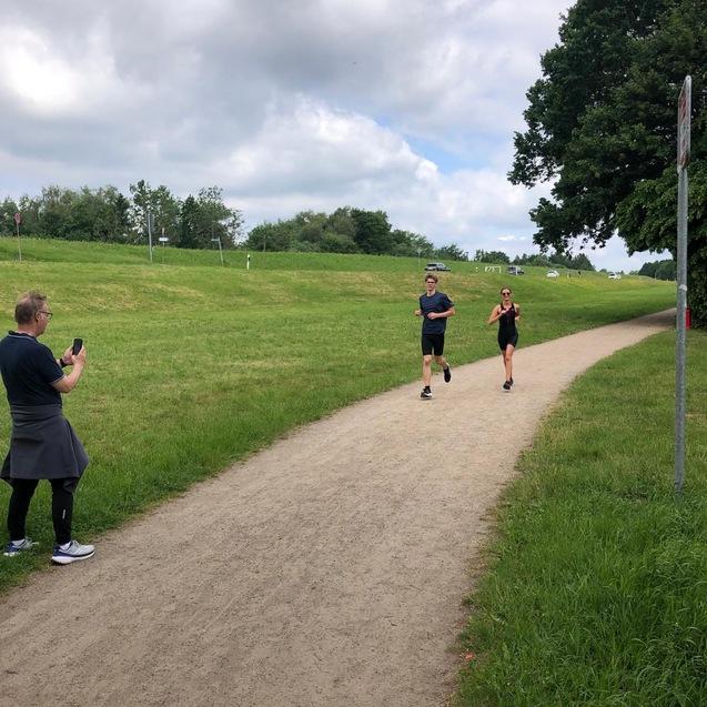 Probetriathlon 2026 Zwei Läufer auf der Strecke laufen auf ein am Wegrand stehende Person zu.
