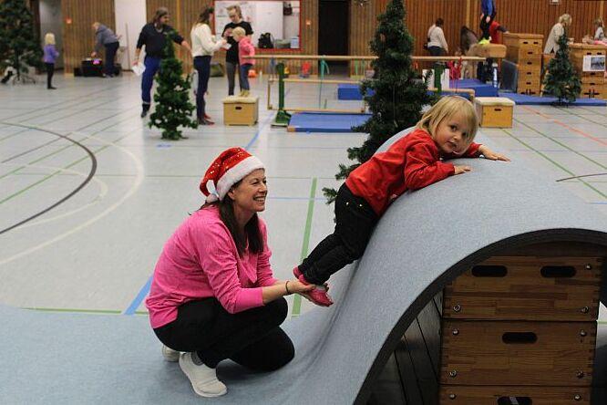 Weihnachtsturnen 2023 Mandy Gellentin mit Weihnachtsmütze hält Kind an den Füßen. Das Kind liegt auf der Matte die sich über einen großen Kasten zieht.