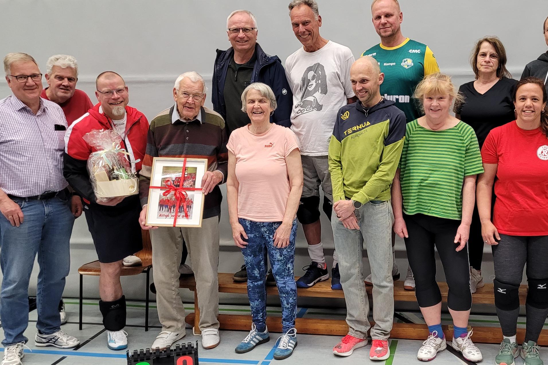 Gruppenfoto mit ungef&auml;hr 14 Personen, die in einer Sporthalle stehen. Uli Tiburg h&auml;lt ein Geschenk in der Hand