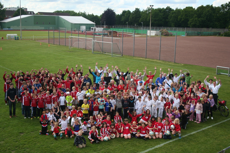 Personen stehen auf dem Rasenplatz und strecken die H&auml;nde in die H&ouml;he