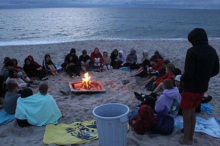 Die Gruppe des Zeltlagers sitzt am Strand um ein Lagerfeuer.