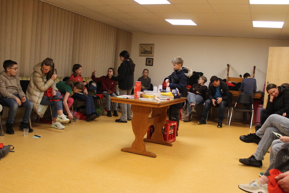 Kinder und Jugendliche sitzen in einem Stuhlkreis. In der Mitte steht ein Tisch mit Essen und Getränken.