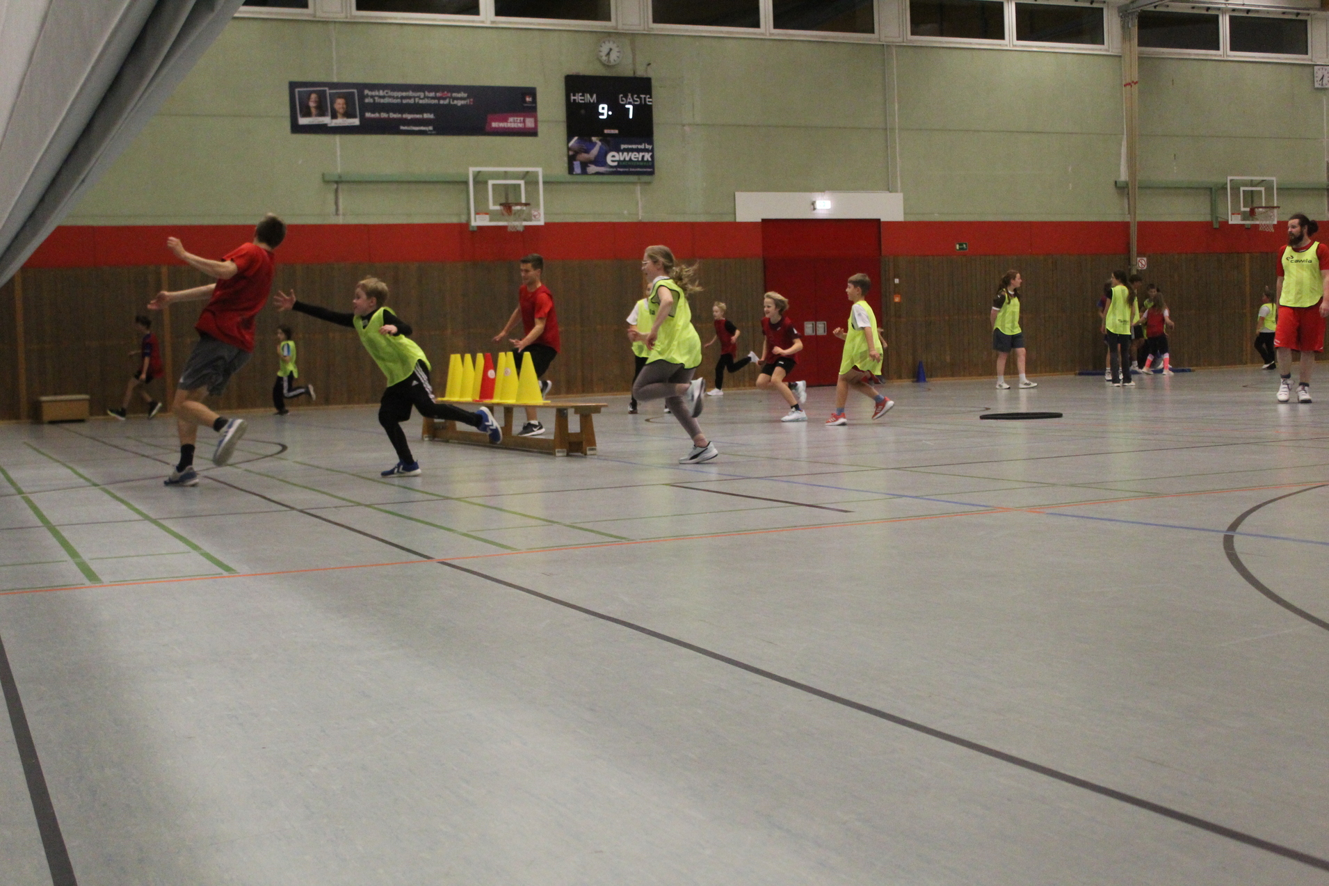 Drei Spieler der roten Mannschaft versuchen, der gelben Mannschaft ein Hütchen von ihrer Turnbank zu klauen. Die gelbe Mannschaft versucht, die roten Spieler zu ticken.