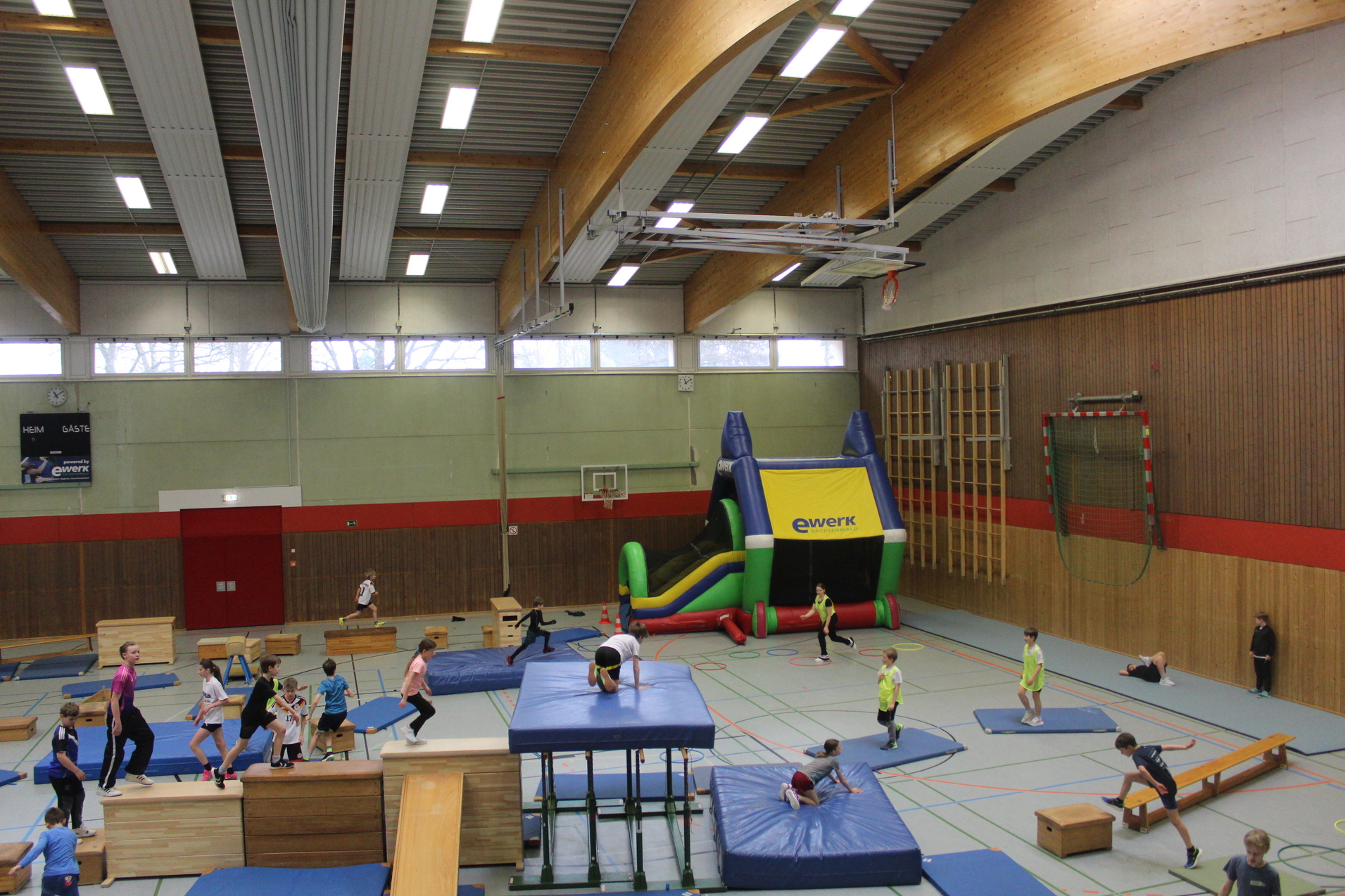 Sporthalle, in der Sportger&auml;te, Weichbodenmatten und K&auml;sten aufgebaut sind. Kinder toben in der Sporthalle