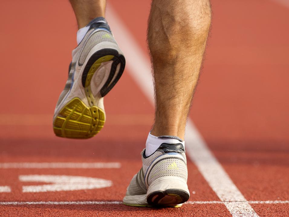Nahaufnahme eines Läufers auf einem roten Laufbahnbelag, der gerade aufsetzt. Sportschuh mit sichtbarem Profil.