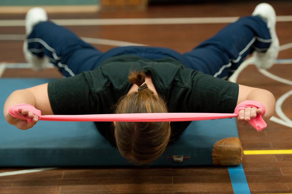 Frau führt eine Übung mit einem pinken Widerstandsband auf einer Matte in einem Sportbereich aus.