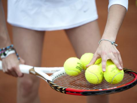 Hand greift mehrere gelbe Tennisbälle auf einem Tennisschläger, während die andere Hand die Schlägerhaltung stabilisiert.