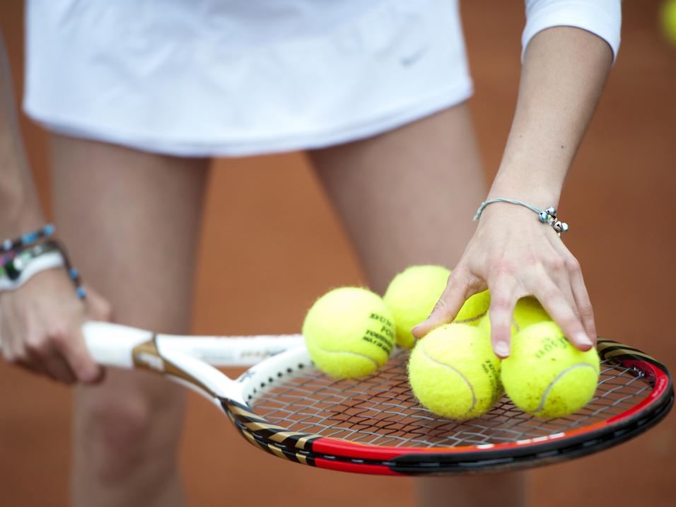 Hand greift mehrere gelbe Tennisbälle auf einem Tennisschläger, während die andere Hand die Schlägerhaltung stabilisiert.