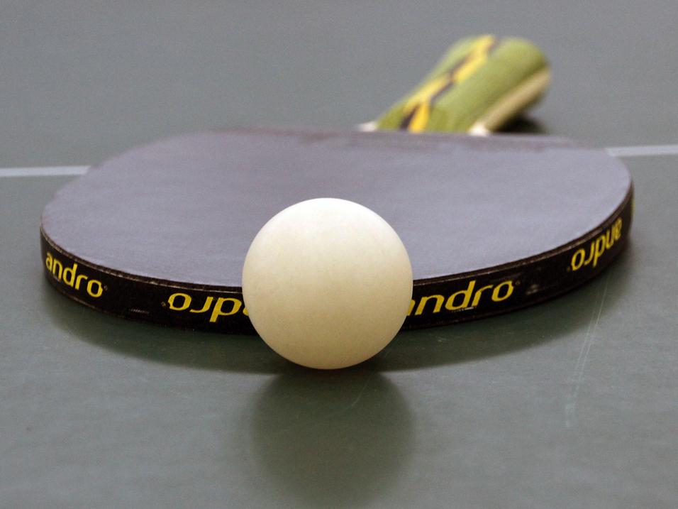 Nahaufnahme eines Tischtennisschlägers mit weißem Ball auf einer grünen Tischtennisplatte.