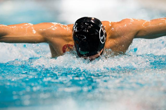 Schwimmer im Wasser führt einen Schmetterlingsschwimmzug aus, eine Hand nach vorne gestreckt, Wassertropfen spritzen.